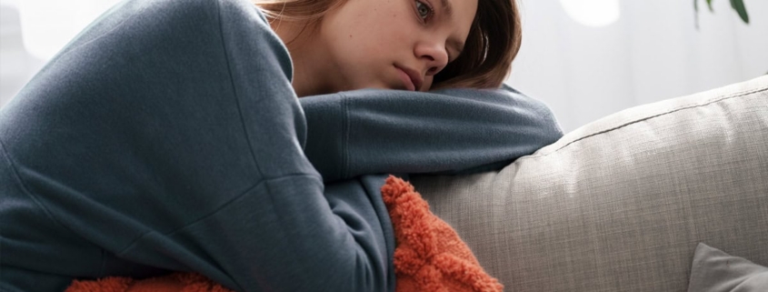 Depressed young woman resting on sofa, feeling unwell or tired, indoor emotional health concept, relaxation and wellness, comfort at home.