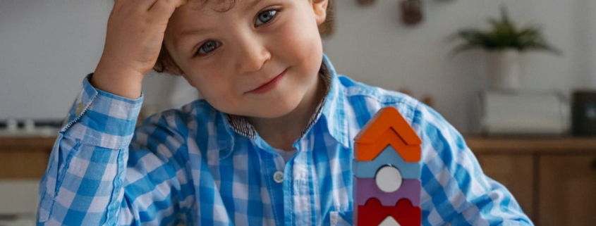 Giovane bambino che gioca con torri di blocchi colorati in cucina, immagini di gioco e creatività infantile, ambiente domestico accogliente e sicuro, stimolazione mentale e sviluppo delle capacità motorie.
